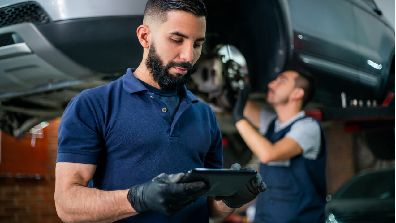  Mechanic using a tablet near an elevated car, illustrating asset management in automotive repair operations.