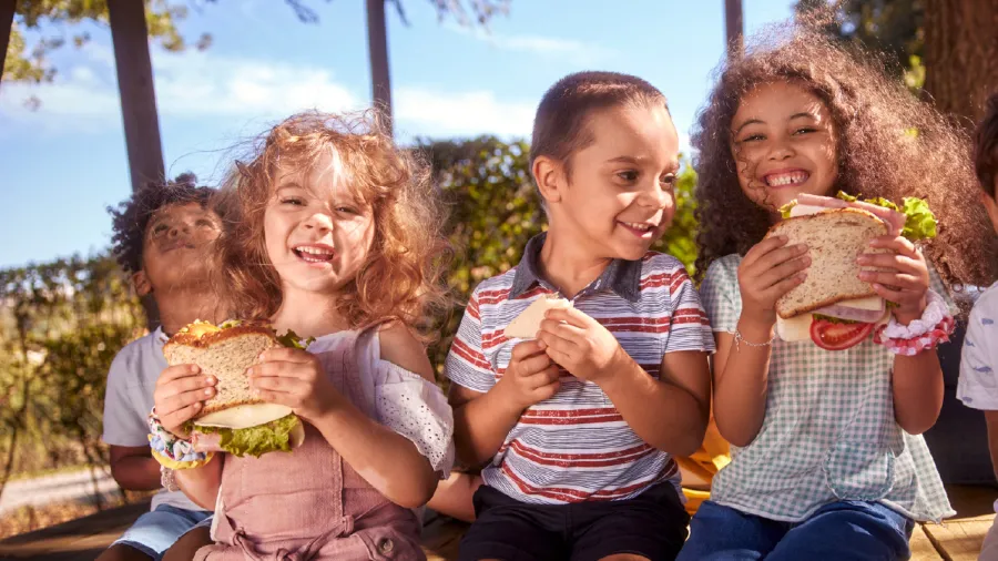  Children eating sandwiches outdoors, highlighting the importance of efficient food supply chain asset management systems