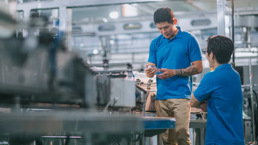  Workers discussing machine operations on factory floor, showcasing the role of predictive asset management tools