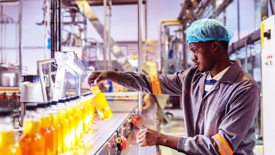  Operator inspecting filled beverage bottles on conveyor belt, optimized by real-time asset monitoring software