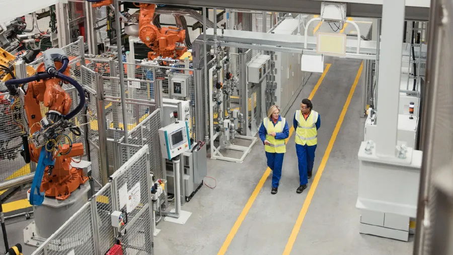  Employees walking in robotic assembly plant, demonstrating how asset management software improves workflow efficiency